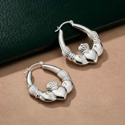 Sterling Silver Large Hoop Claddagh Earrings on a beige surface with a dark green background