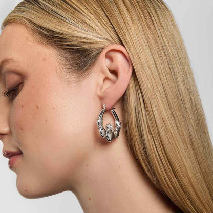 Close-up of a woman wearing Sterling Silver Large Hoop Claddagh Earrings 
 on a plain background