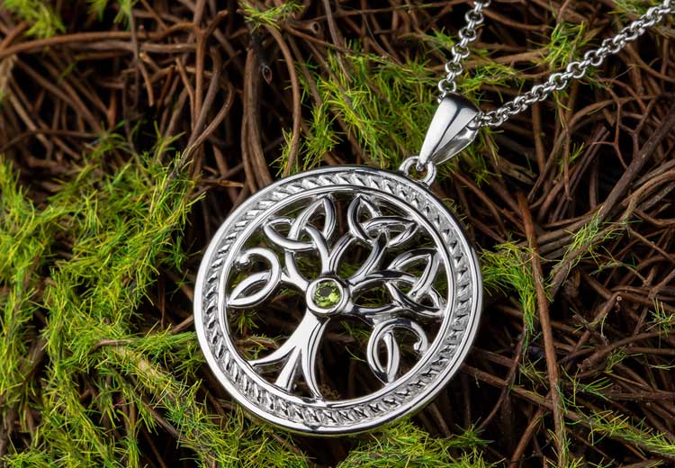 A Sterling Silver Celtic Trinity Knot Necklace with Green crystal at its center on a bed of green moss