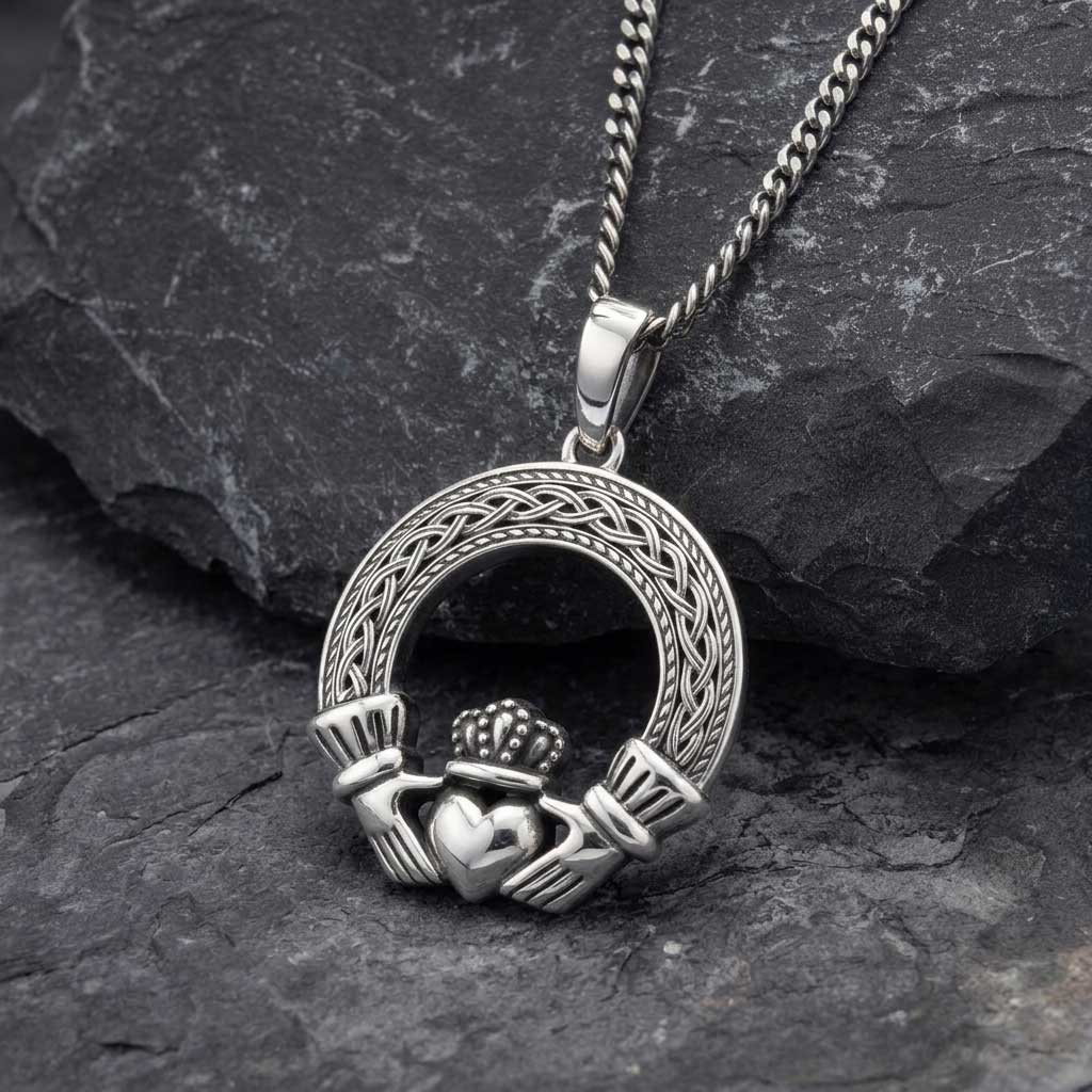 a mens irish jewelry sterling silver celtic claddagh pendant resting on a dark textured slate surface.