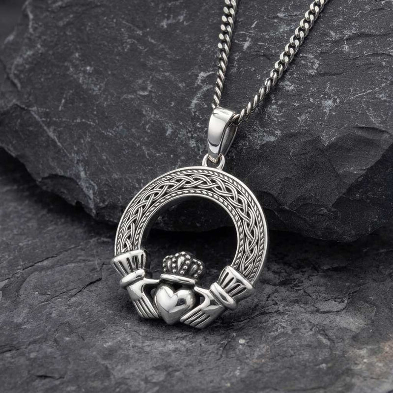 A Mens Irish Jewelry Sterling Silver Celtic Claddagh Pendant resting on a dark textured slate surface.