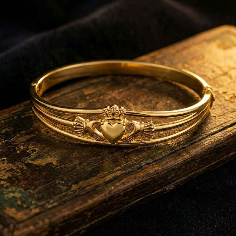 Gold Plated Claddagh Bangle on an aged piece of wood with sunlight reflecting upon it