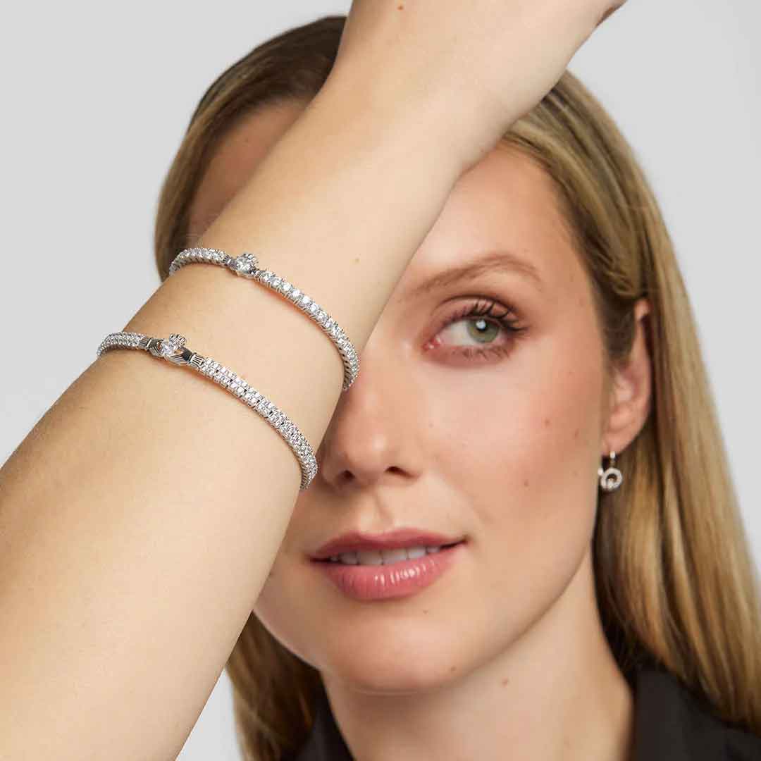 woman with blonde hair wearing two irish claddagh tennis bracelets on a plain background
