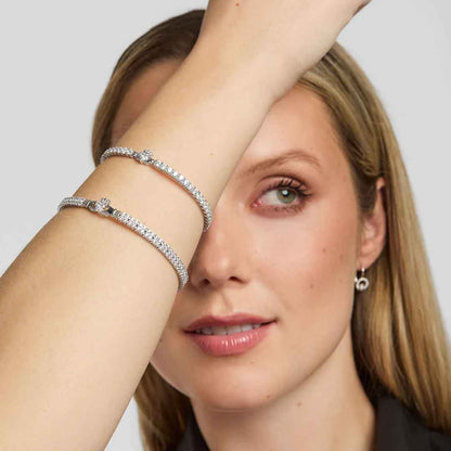 Woman with blonde hair wearing two Irish Claddagh Tennis bracelets on a plain background