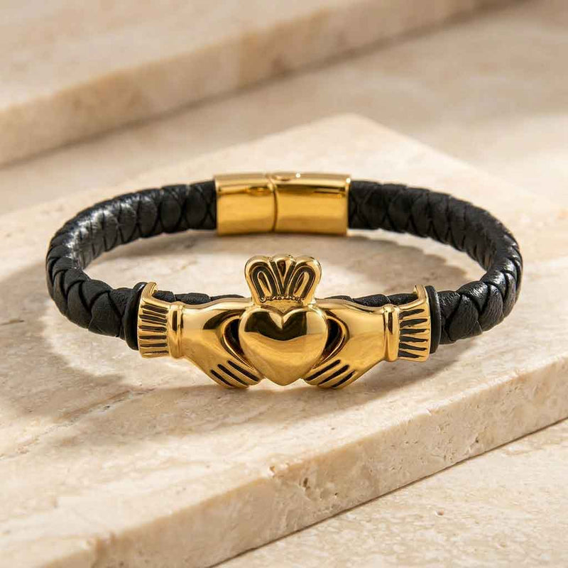 Gold Plated Leather Mens Claddagh Bracelet on a white background on a light stone surface