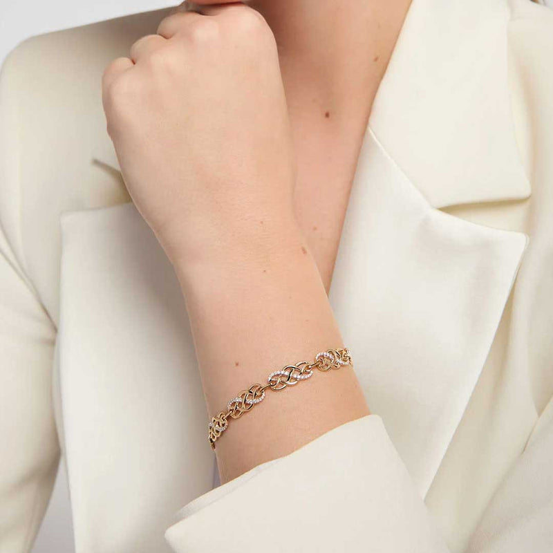 A close-up of a woman wearing an Irish 14k Gold Diamond Celtic Knot Bracelet, styled with a cream-colored blazer.