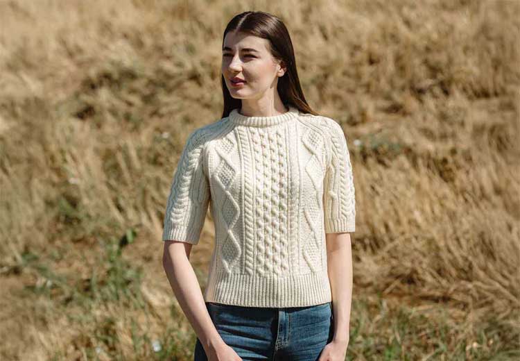 Woman wearing a natural colored Ladies Cable Knit Short Sleeve Aran Sweater, standing in a field