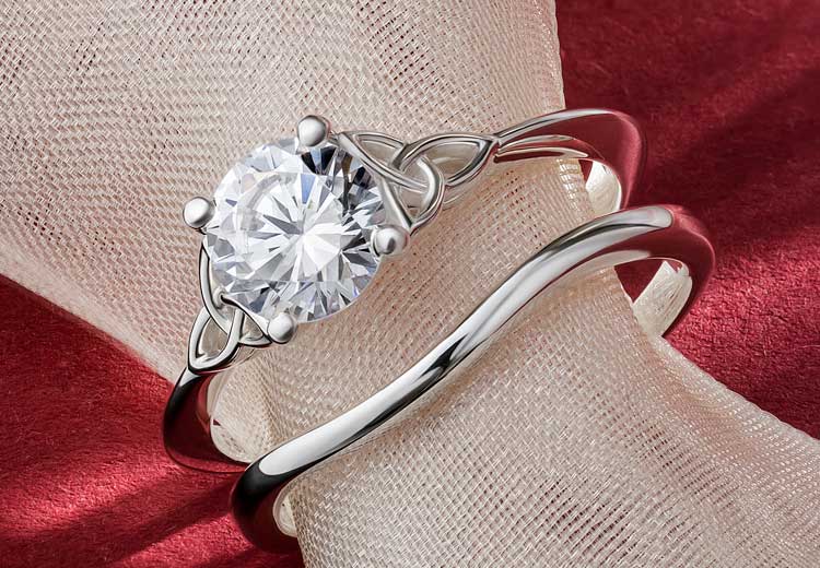 White Gold Diamond Irish Trinity Knot Wedding Ring and matching wishbone band on a red background