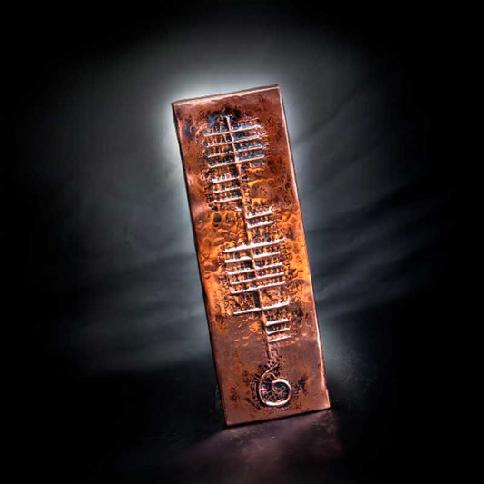 Copper plaque with embossed Ogham Gaelic Text and celtic design in front of a black backdrop
