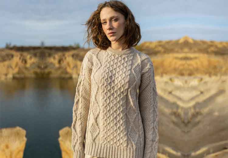 Woman in an Irish Fisherman Cable Knit Ladies Sweater standing by a lake with a blurred background