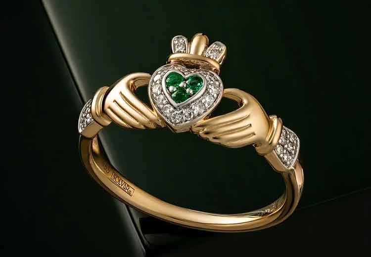 Gold Claddagh ring with heart-shaped emerald and diamonds on a black background