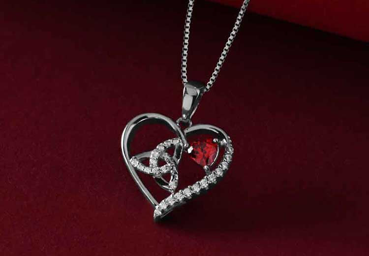 Heart-shaped Sterling Silver Irish Trinity Knot Necklace with a red gemstone on a dark red background